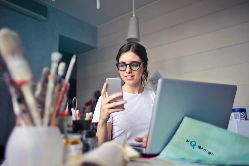 A girl looking at her phone in front of a laptop